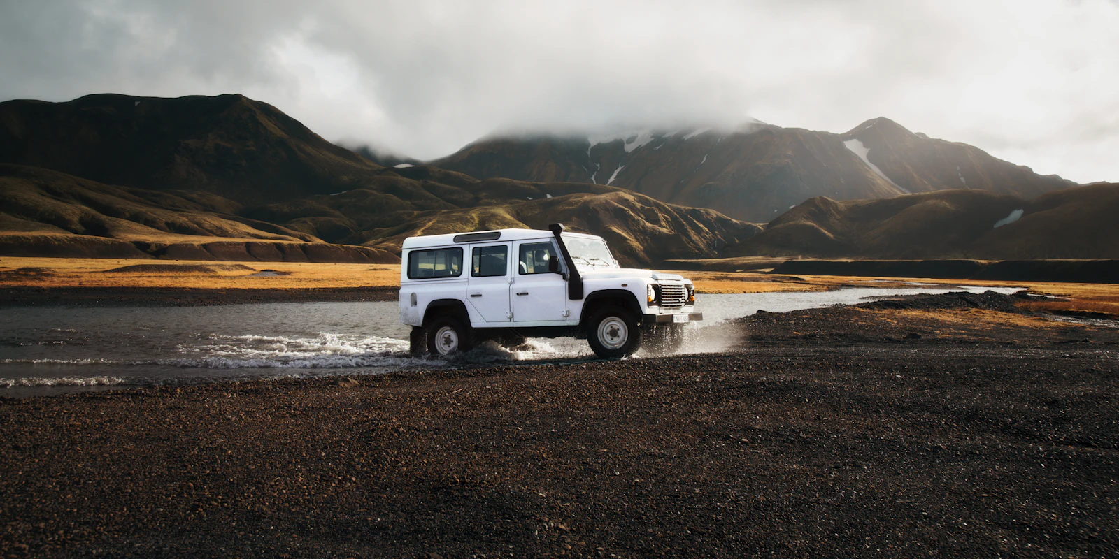 White Land Rover Defender crossing shallow water in Iceland